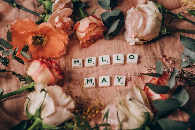 Hello May spelled out with scrabble tiles surrounded by pink flowers