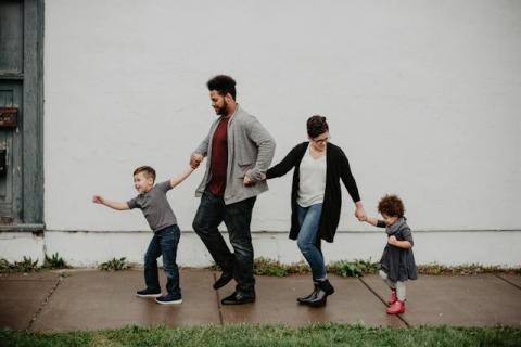 Two adults, a man and a woman, holding hands with two children, walking down a rain covered sidewalk happily