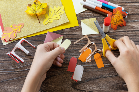 hands cutting out fall colored construction paper