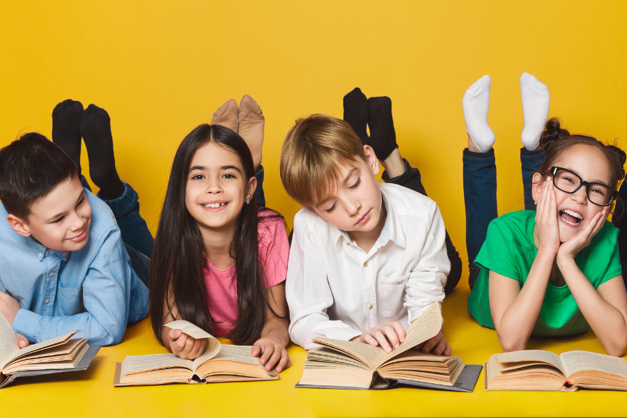 four children laying on the ground reading books