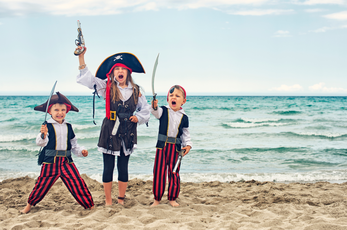 three children dressed as pirates on a beach